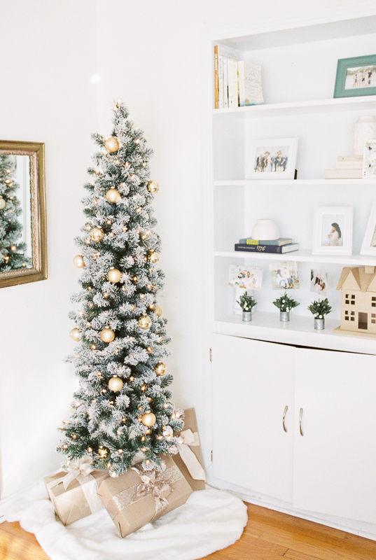 A small lit Christmas tree in front of a white bookcase decorated for Christmas.