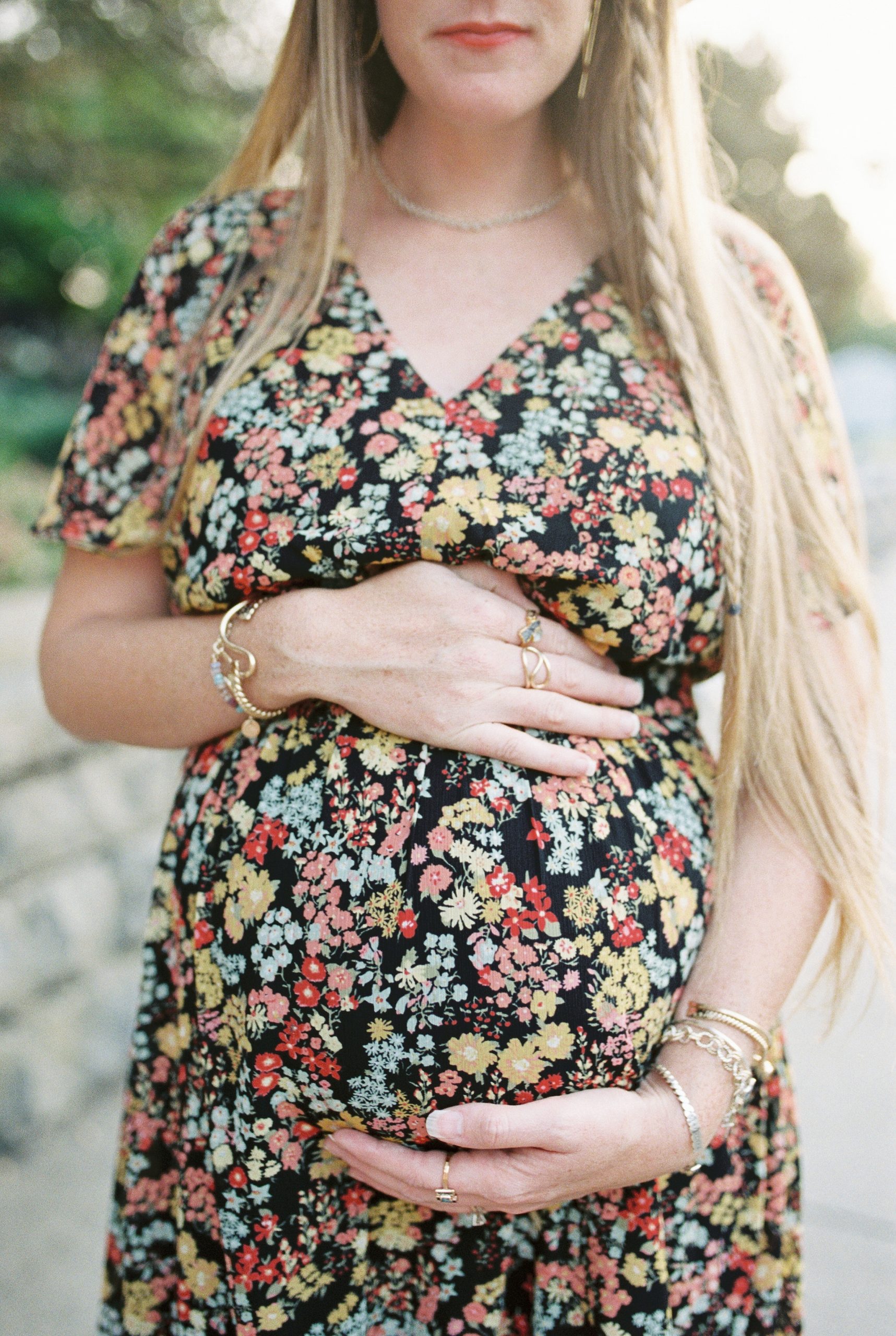 mother in floral dress with gold jewelry shows off baby bump during photoshoot in Downtown Franklin