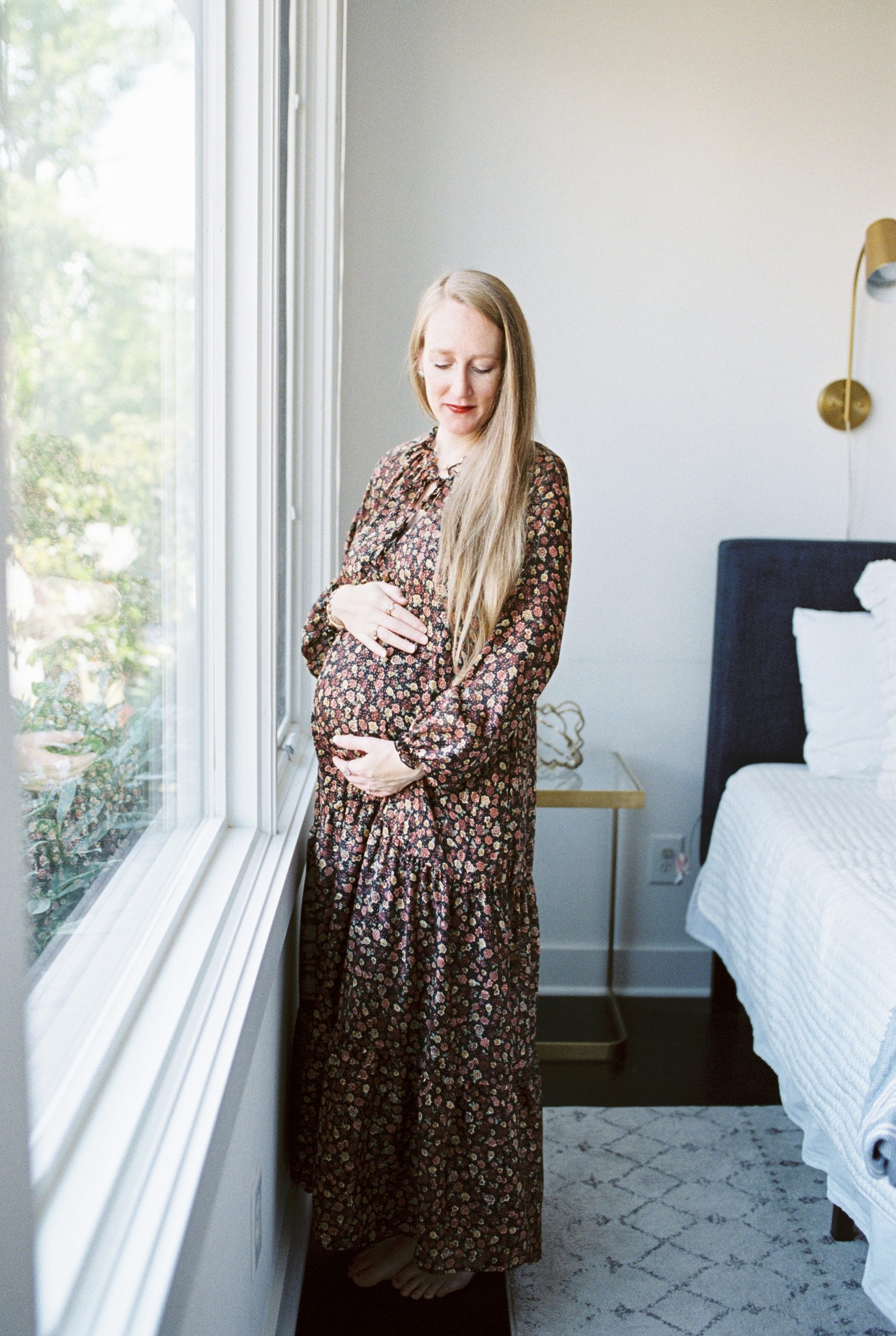 expectant mom standing next to window posing for maternity photos