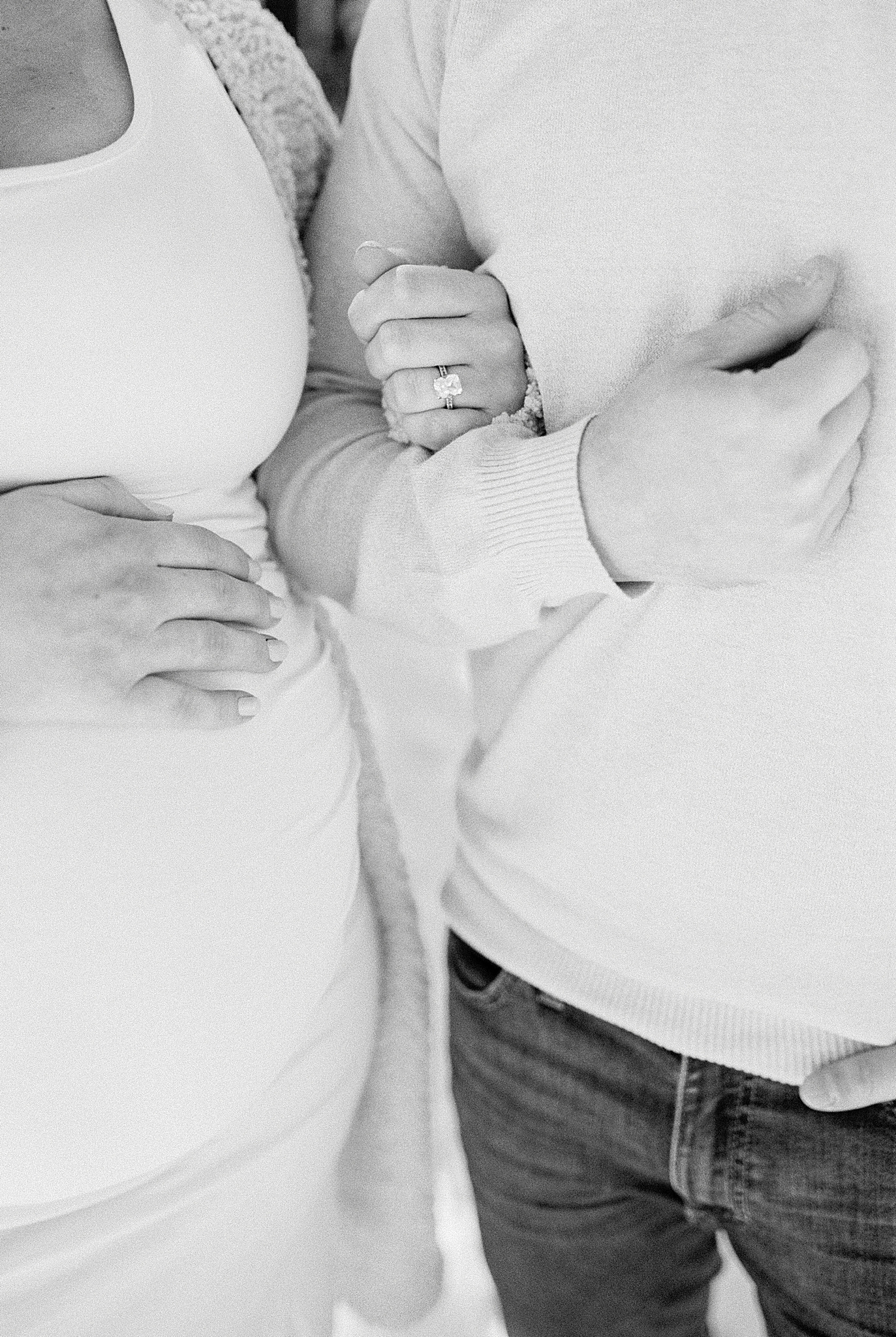 mom holds dad's arm and belly during snowy maternity photos