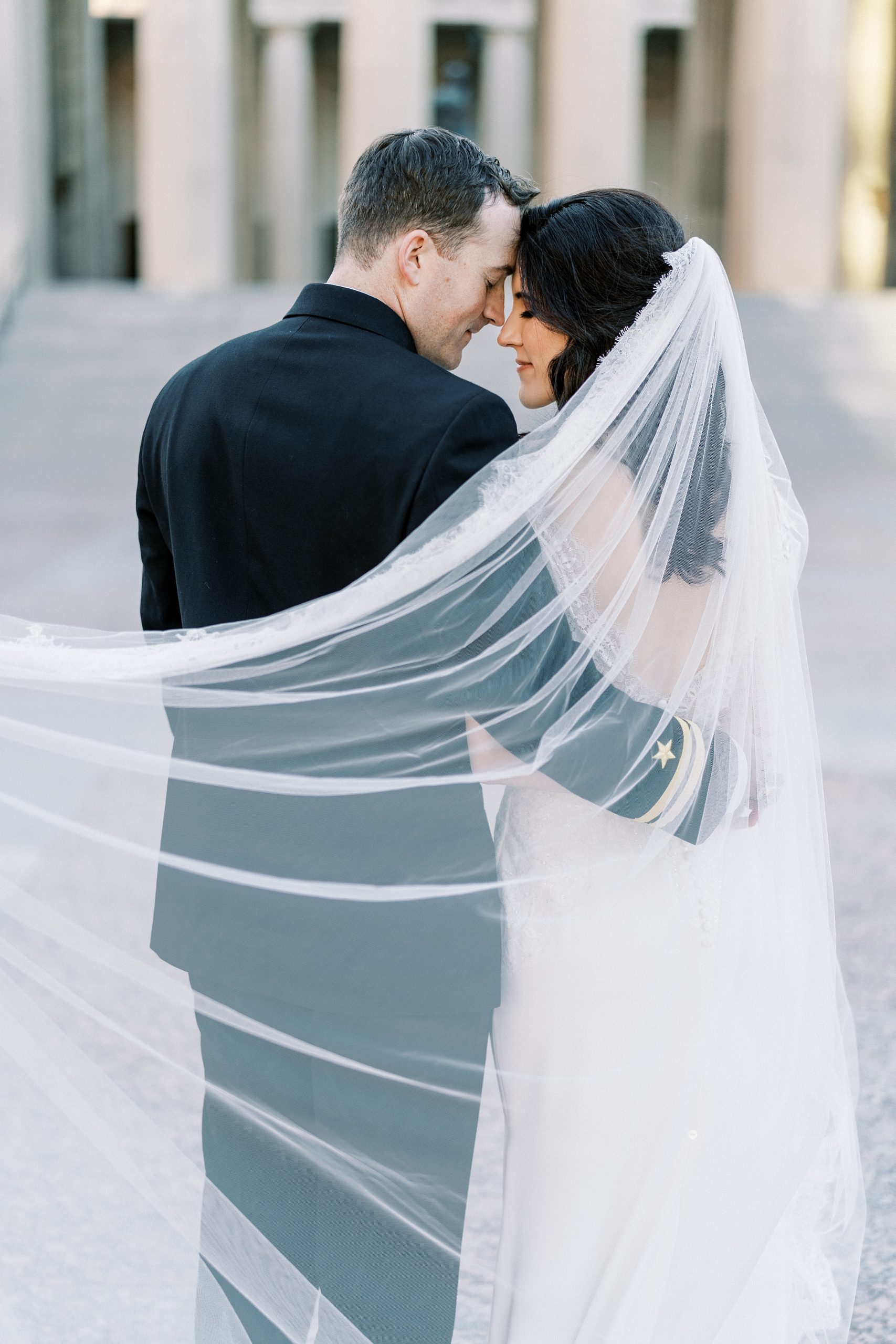 bride and groom nuzzle noes with veil around shoulders