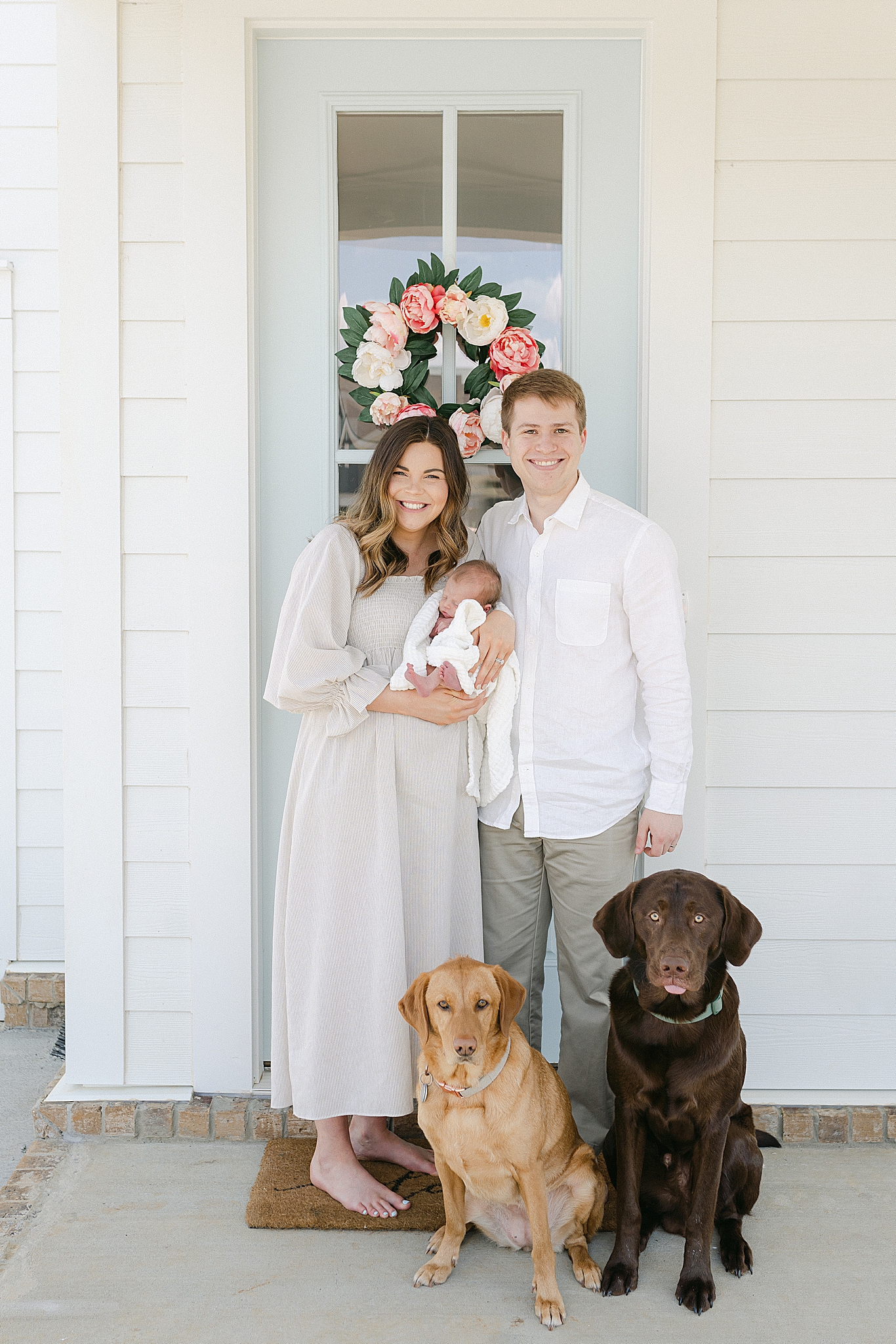 new parents pose with baby and two dogs outside new home