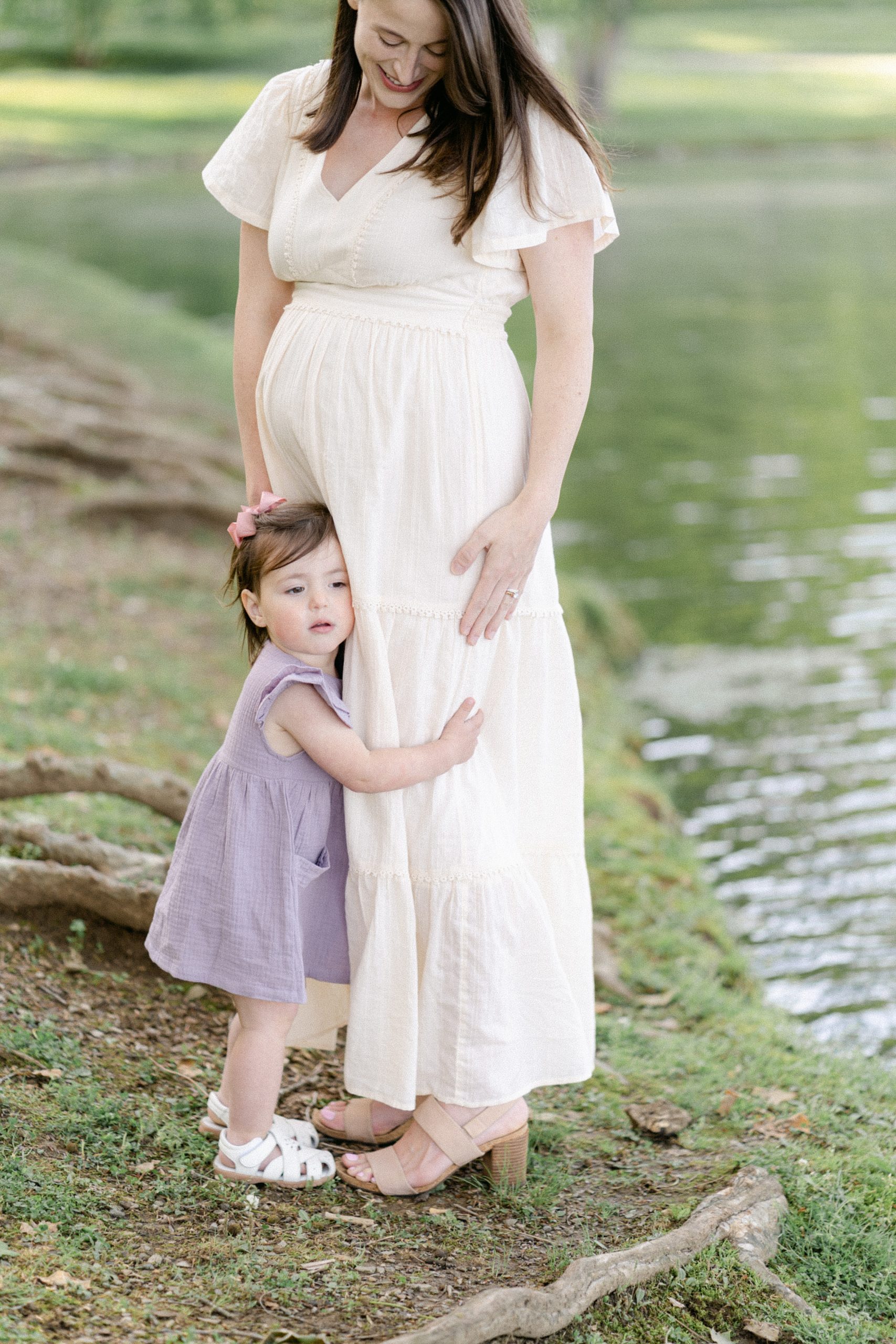 daughter hugs mama's legs by lake during Nashville maternity session