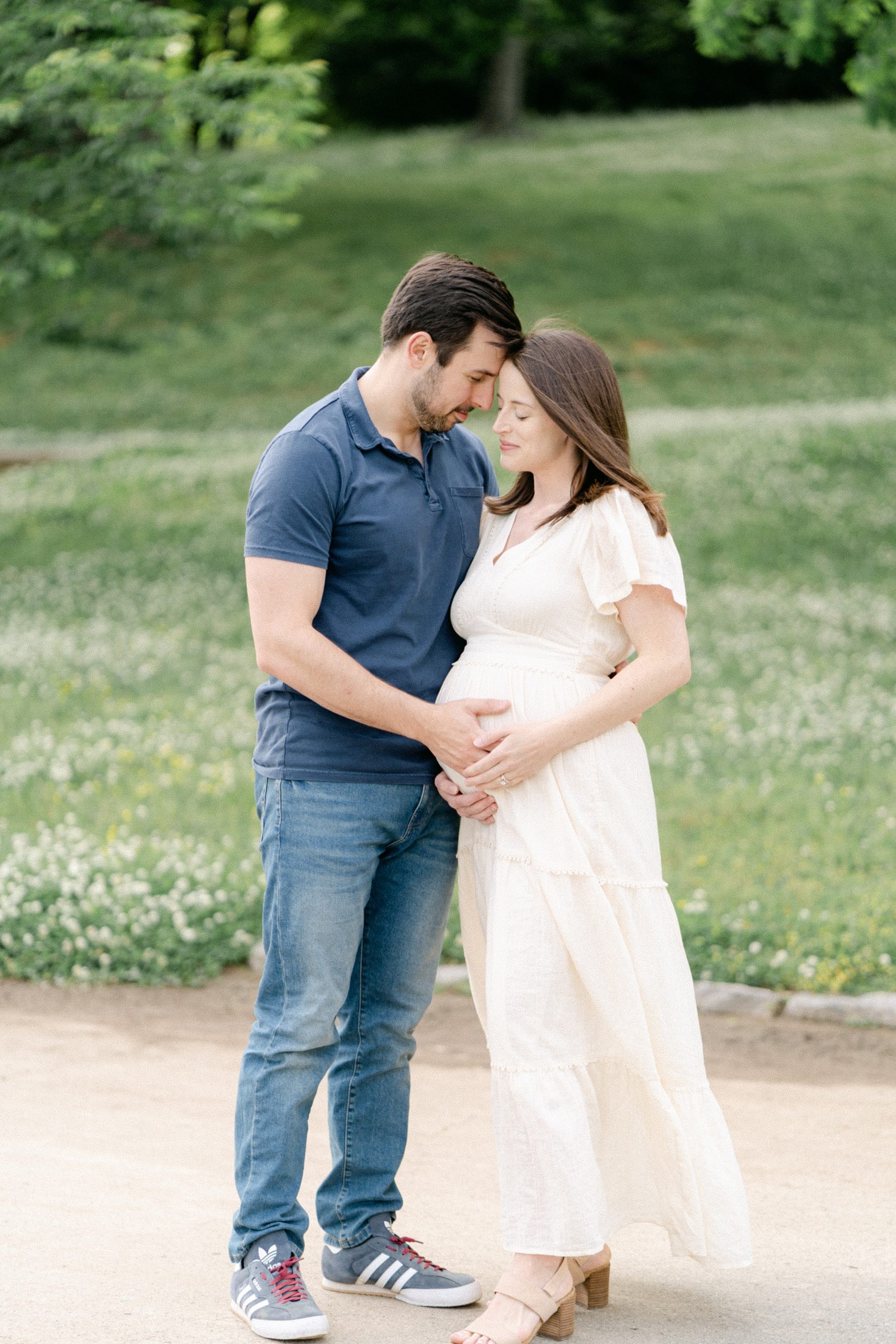 husband and wife lean in close holding belly in maternity session