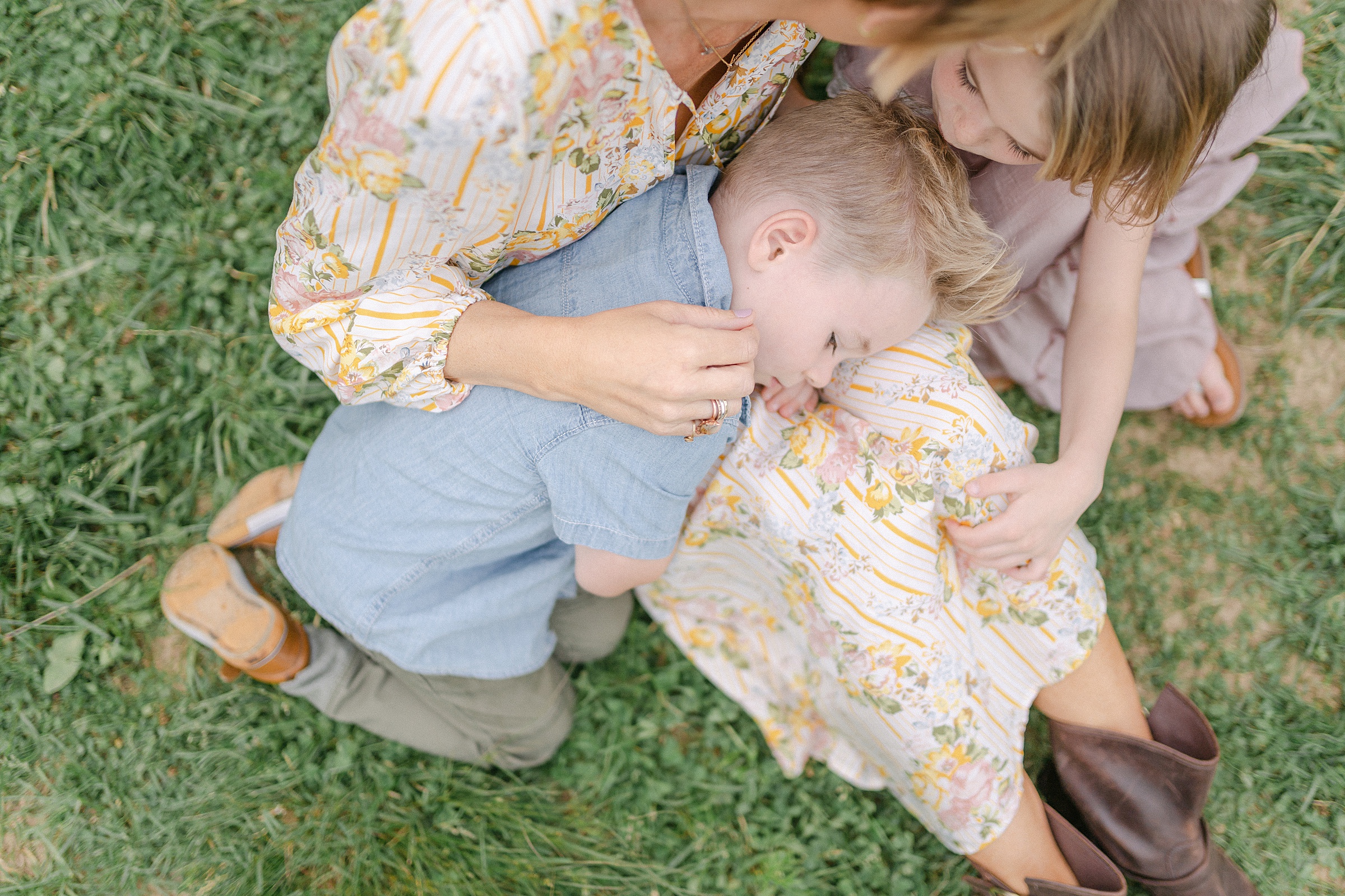 mom holds her two kids close sitting in grass for spring family photos