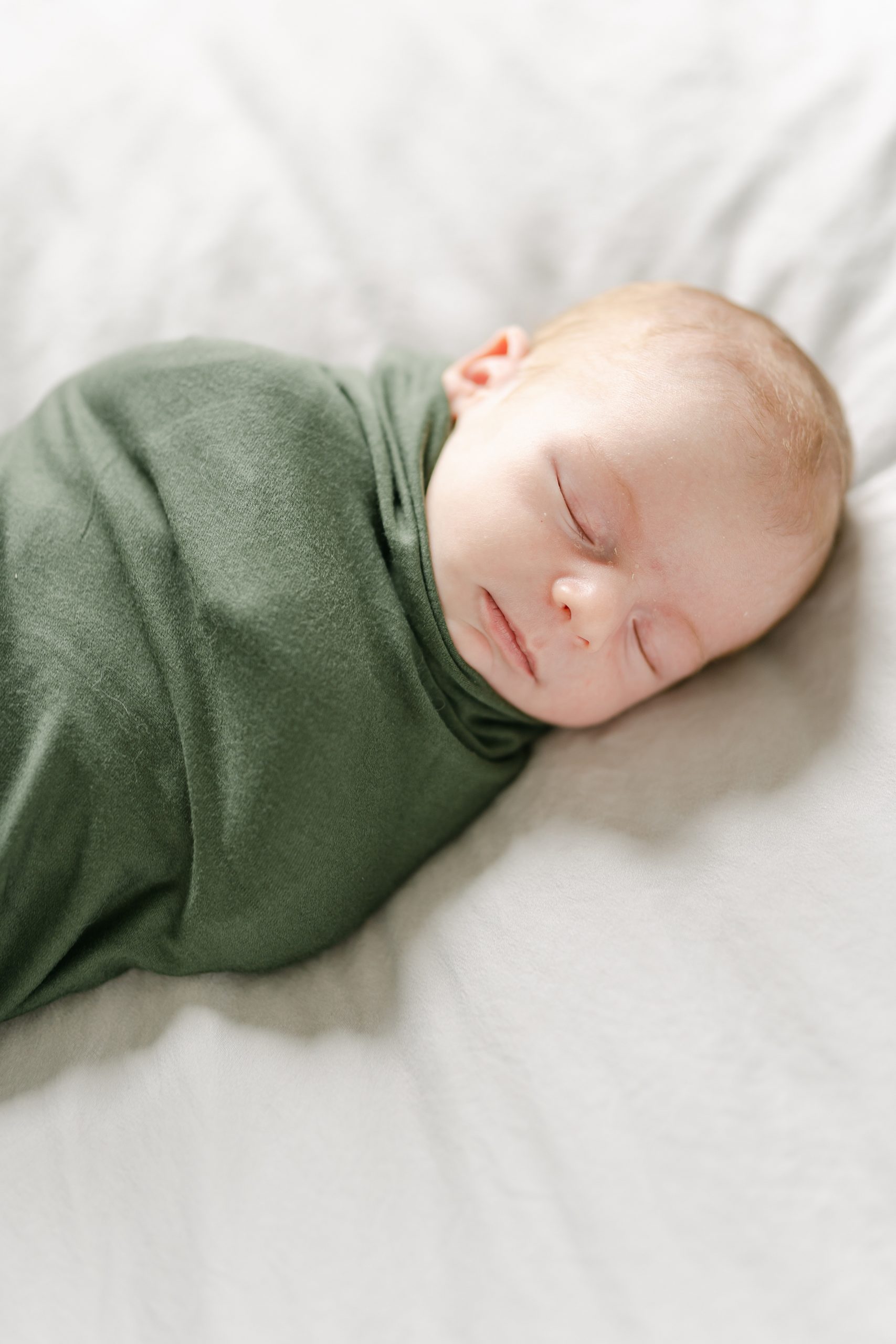 newborn boy wrapped in hunter green blanket during newborn in-home session