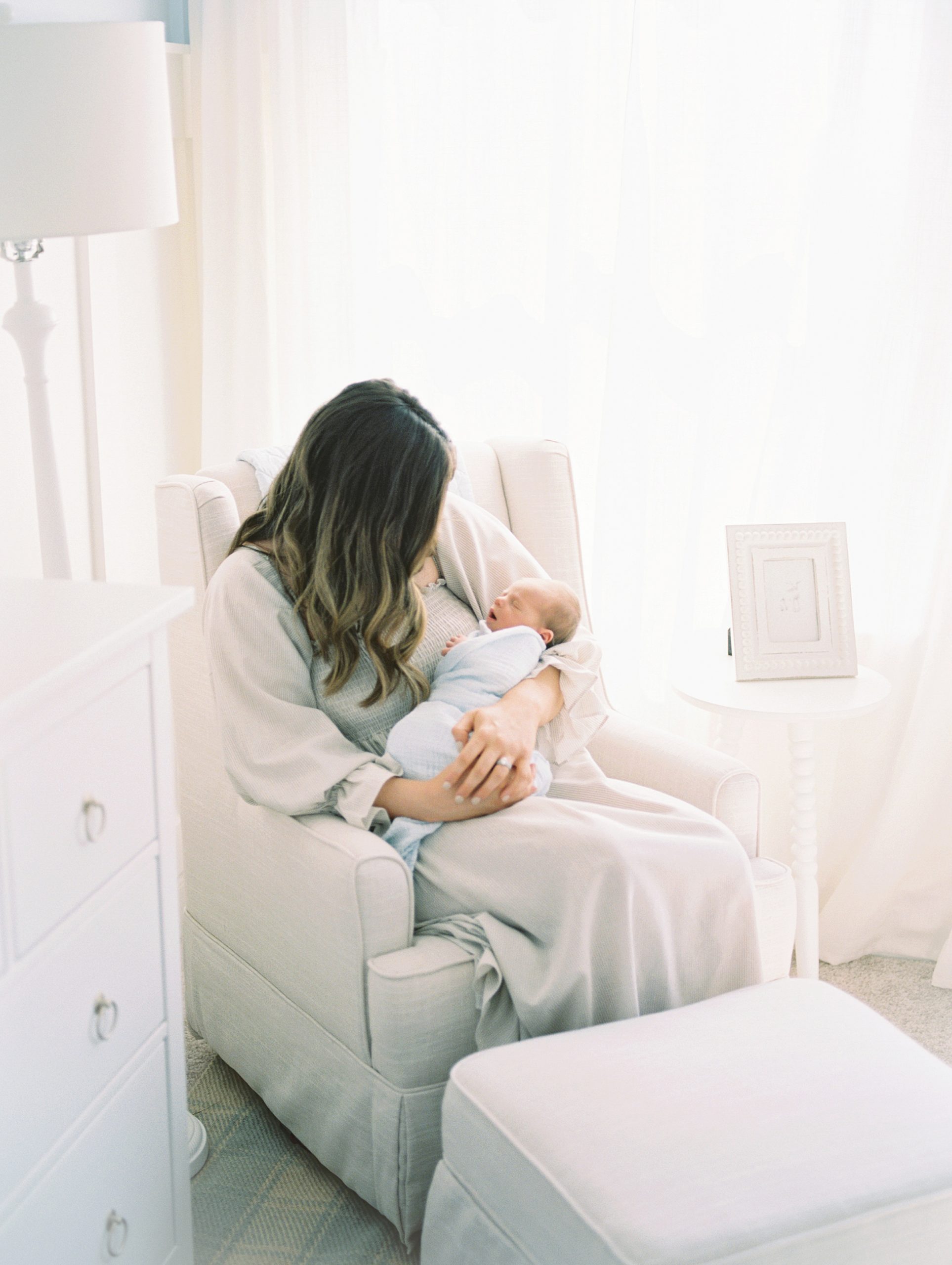 mom sits in glider holding newborn son in nursery