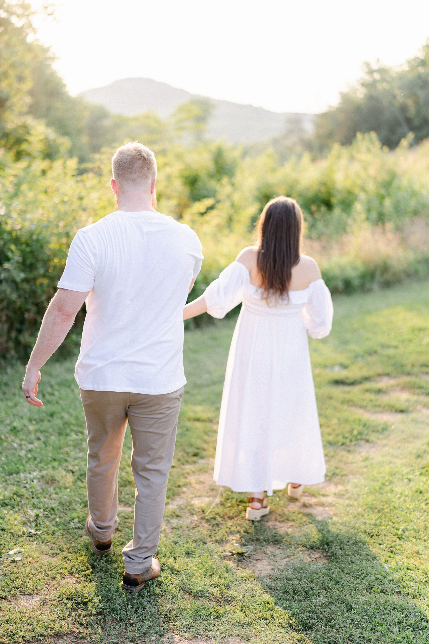 couple holds hands and walks along tall grass of hillside