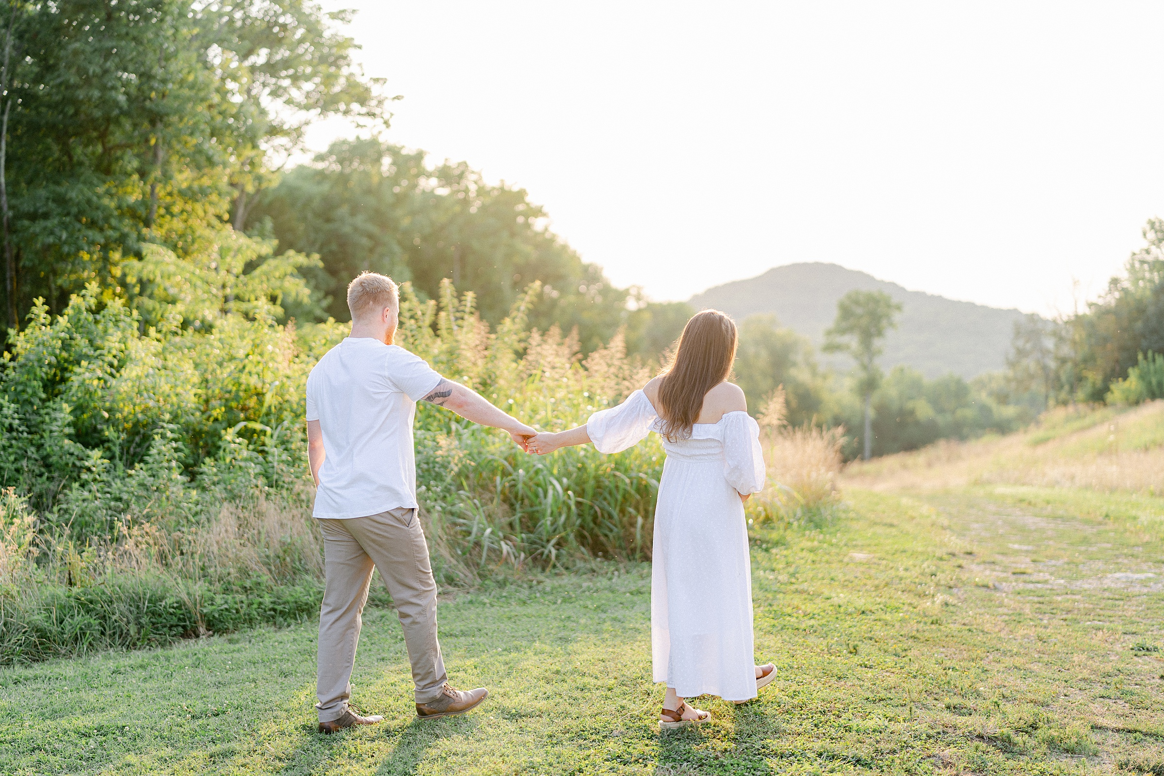 couple holds hands and walks along tall grass of hillside in Brentwood TN