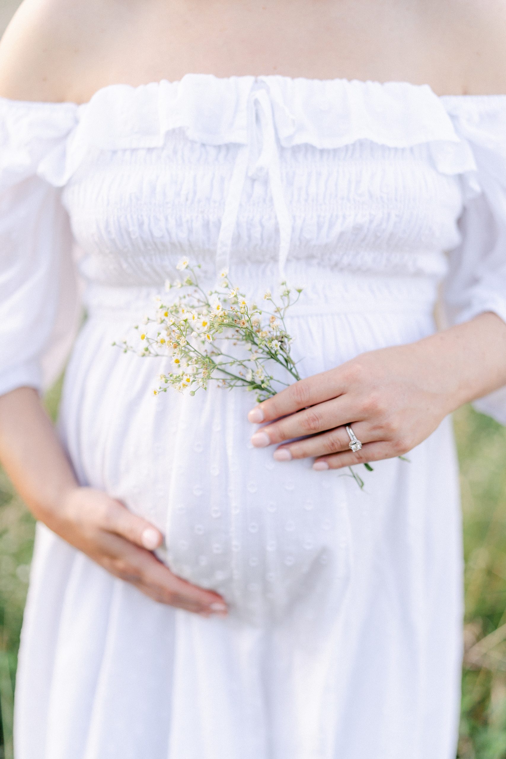 mom to be holds baby belly with white flowers in hand