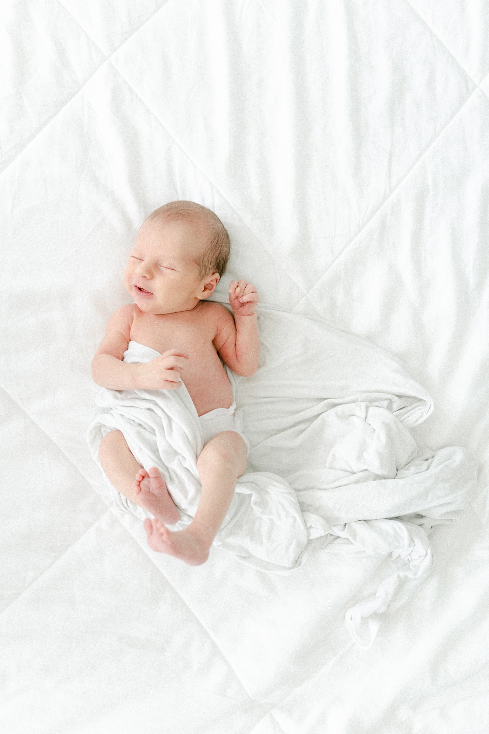 sweet baby boy in while blanket smiles slightly during Newborn portraits