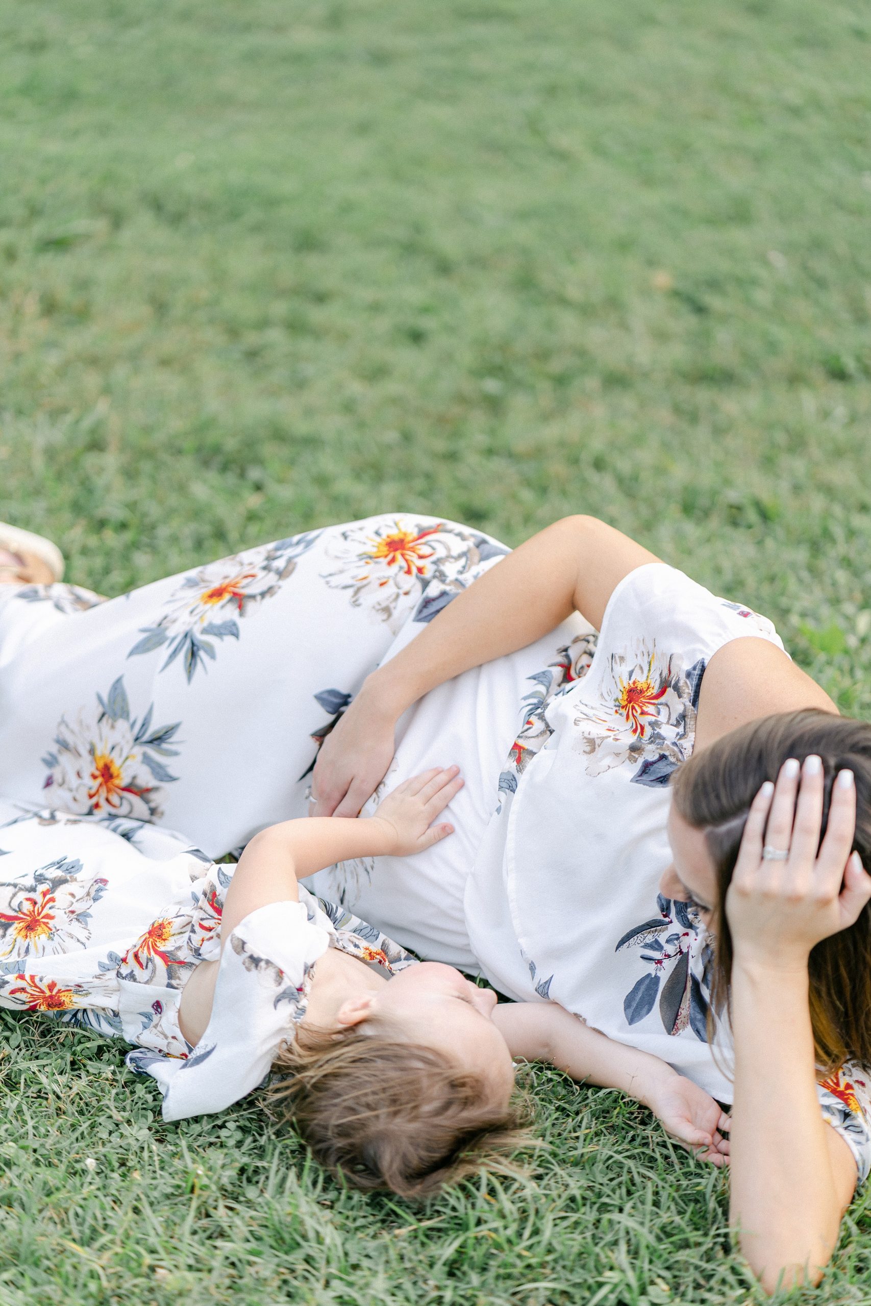 mom and little girl lay in the grass as daughter touches mom's belly during Nashville Maternity session