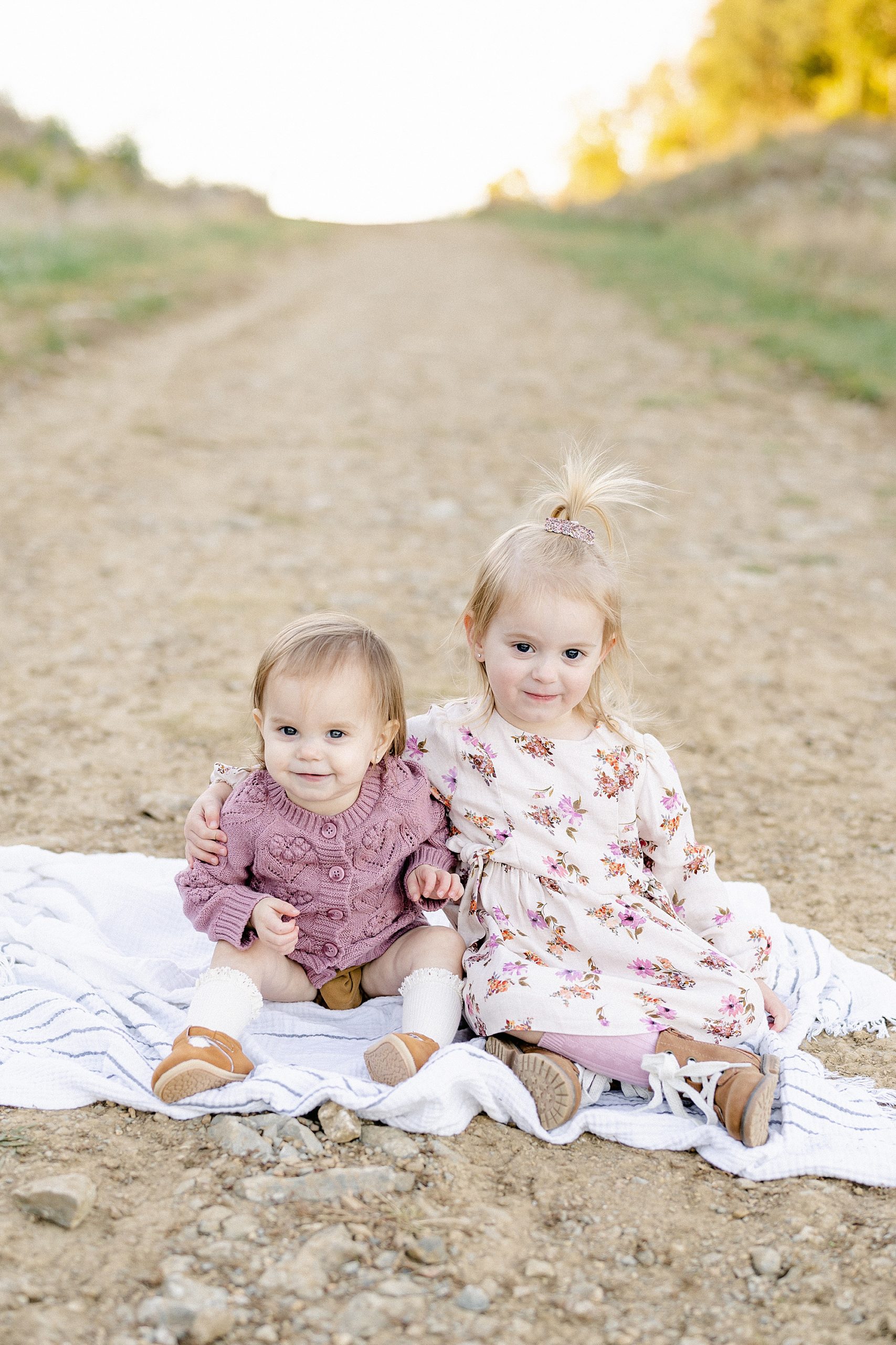 sisters sit on a blanket together during family session