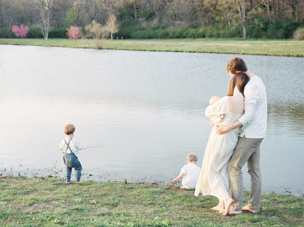 Family walking barefoot by a pond during a summer photo session.