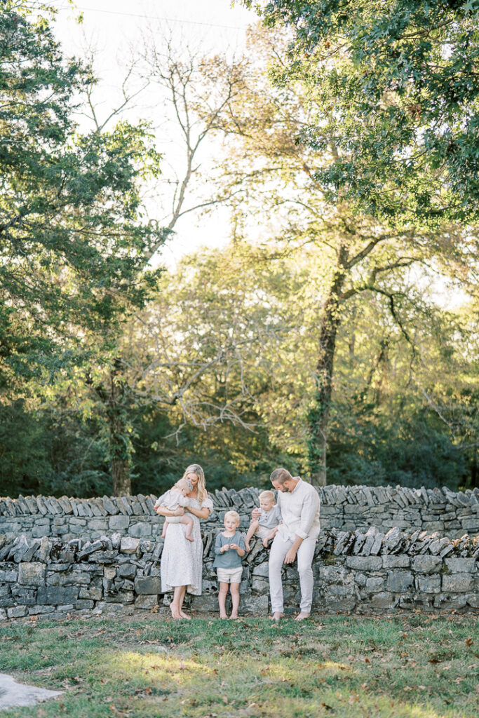 Brentwood family of five sitting in a grove of trees during fall, dressed in creamy neutral outfits.