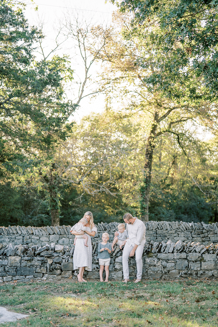 Brentwood family of five sitting in a grove of trees during fall, dressed in creamy neutral outfits.